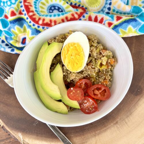 quinoa recipe with turmeric with hard boiled egg, tomatoes and avocado in a bowl