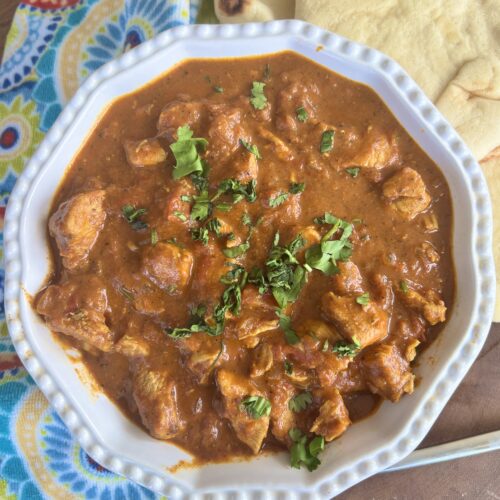 bowl with creamy chicken curry on table with naan bread